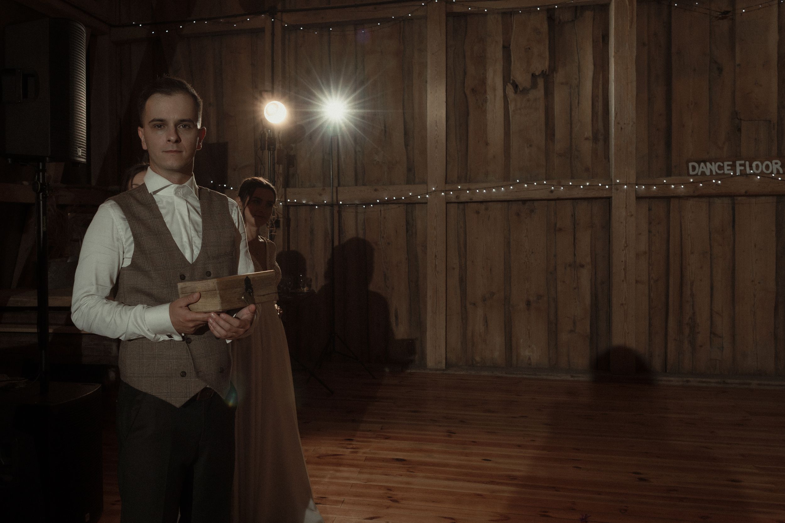A wooden barn interior with rustic beams and warm lighting creates an atmospheric setting for a wedding celebration.