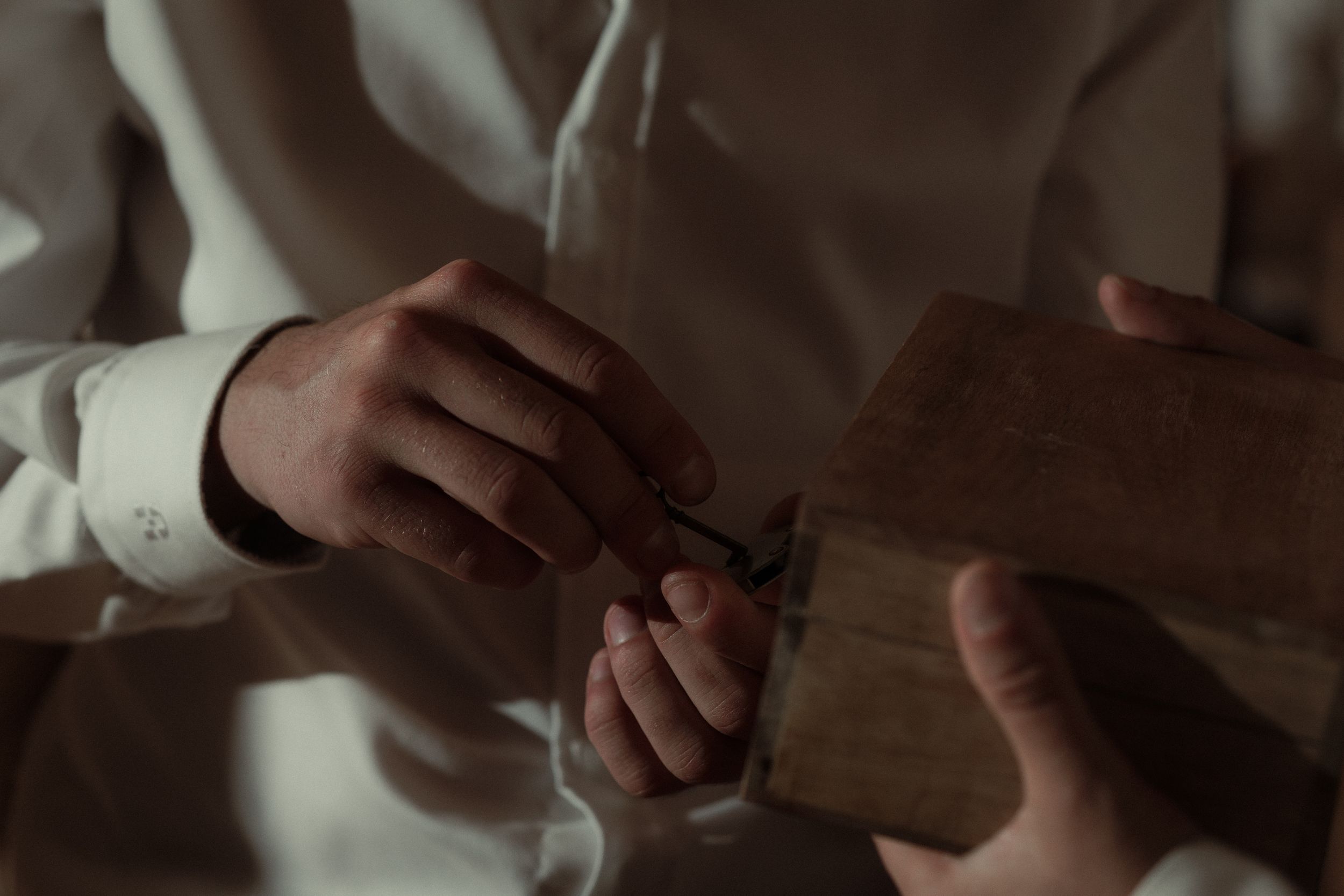 Close up views of hands carefully carving a wooden guitar neck on a workbench with tools and wood shavings.