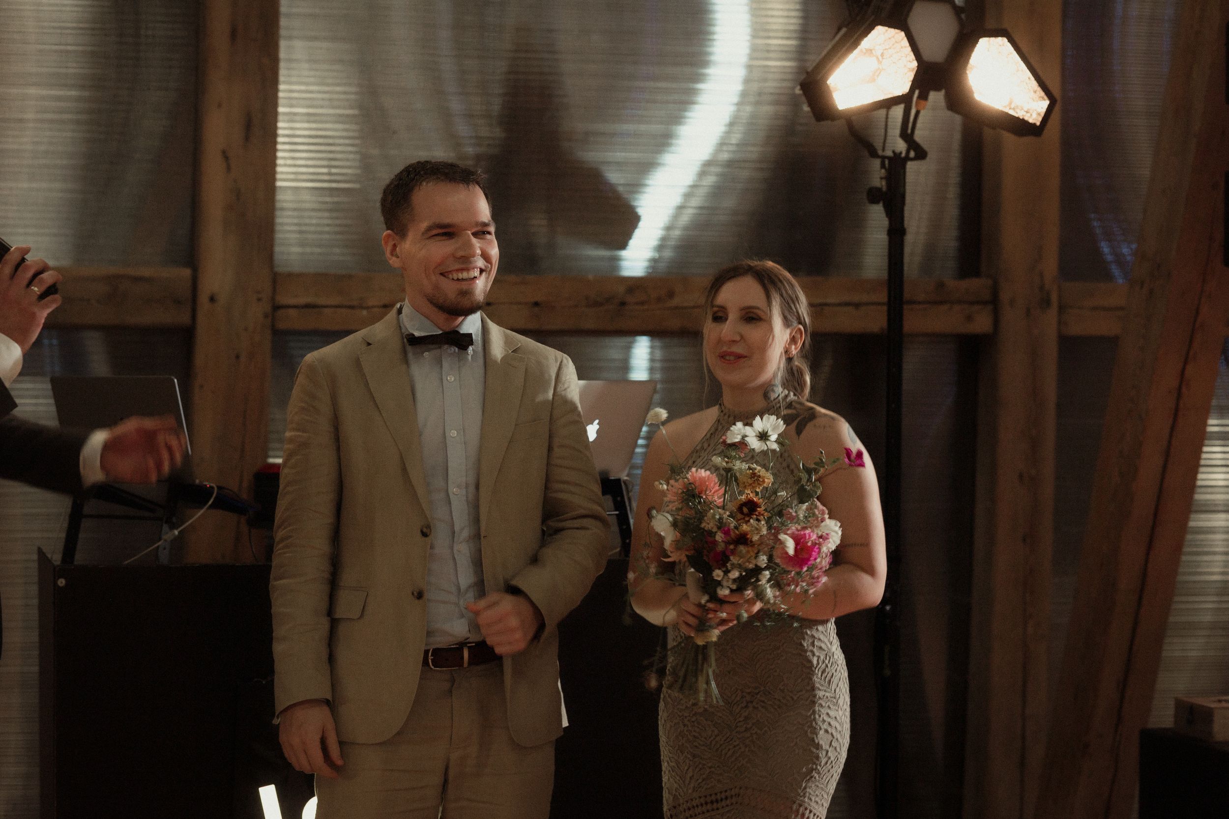 A happy rural wedding celebration outdoors with rustic decor and guests enjoying a toast under strings of lights.