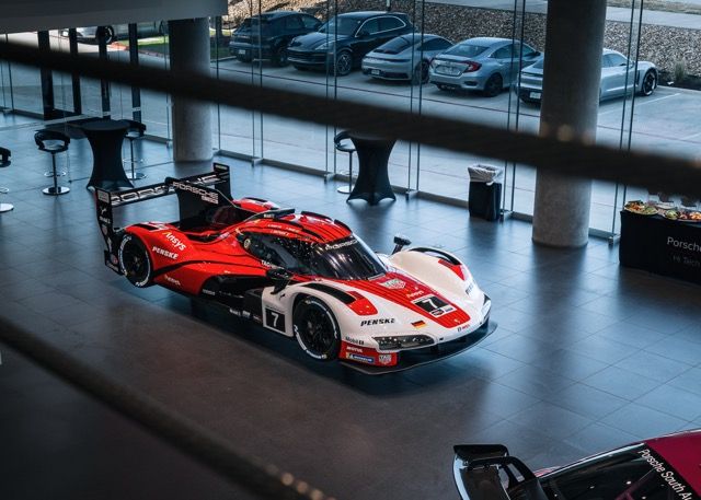 Red racing car on display in modern showroom with glass windows and columns.