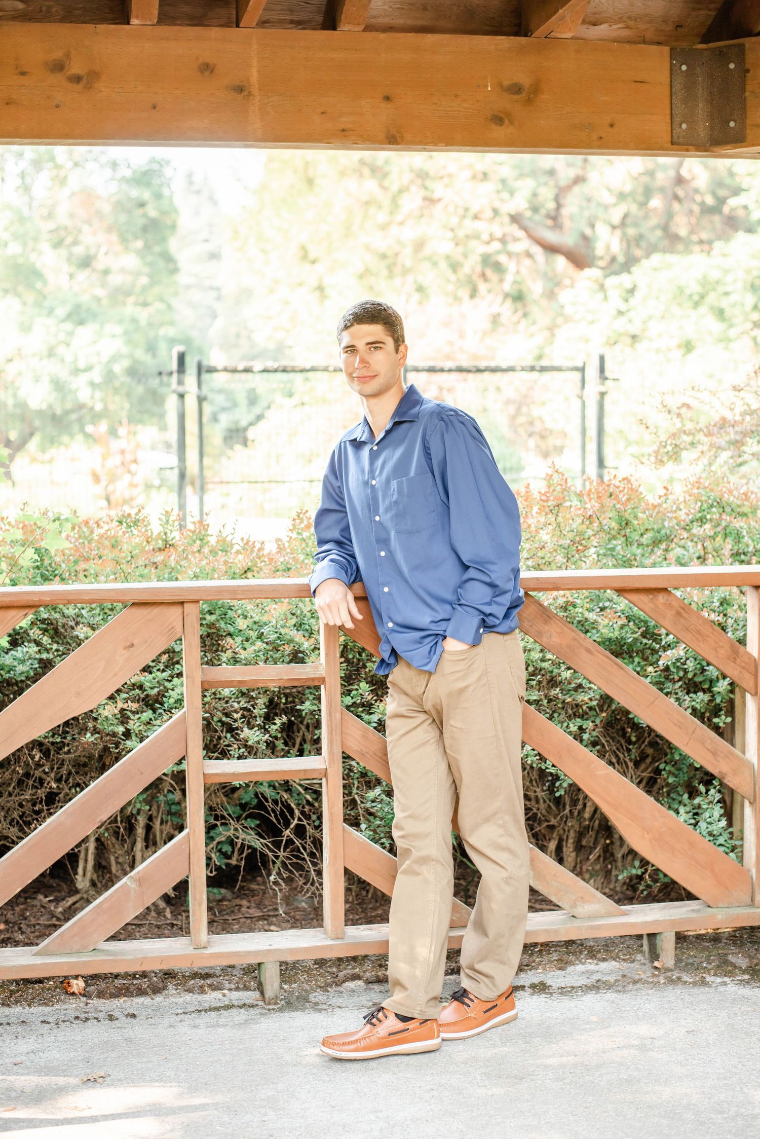 Series of casual poses on a wooden deck railing in a blue button-down shirt and khaki pants.