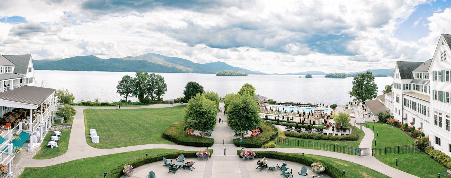 A scenic panoramic view of a lakeside resort property with white buildings and lush green landscaping against mountains.