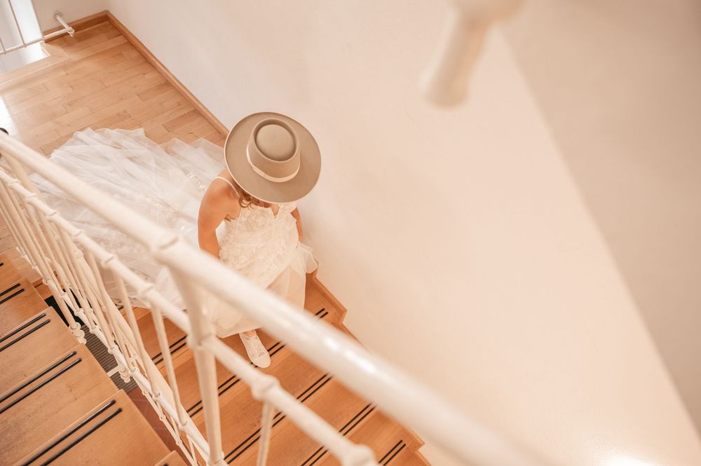 A person wearing a hat descends a white staircase in warm, natural lighting.