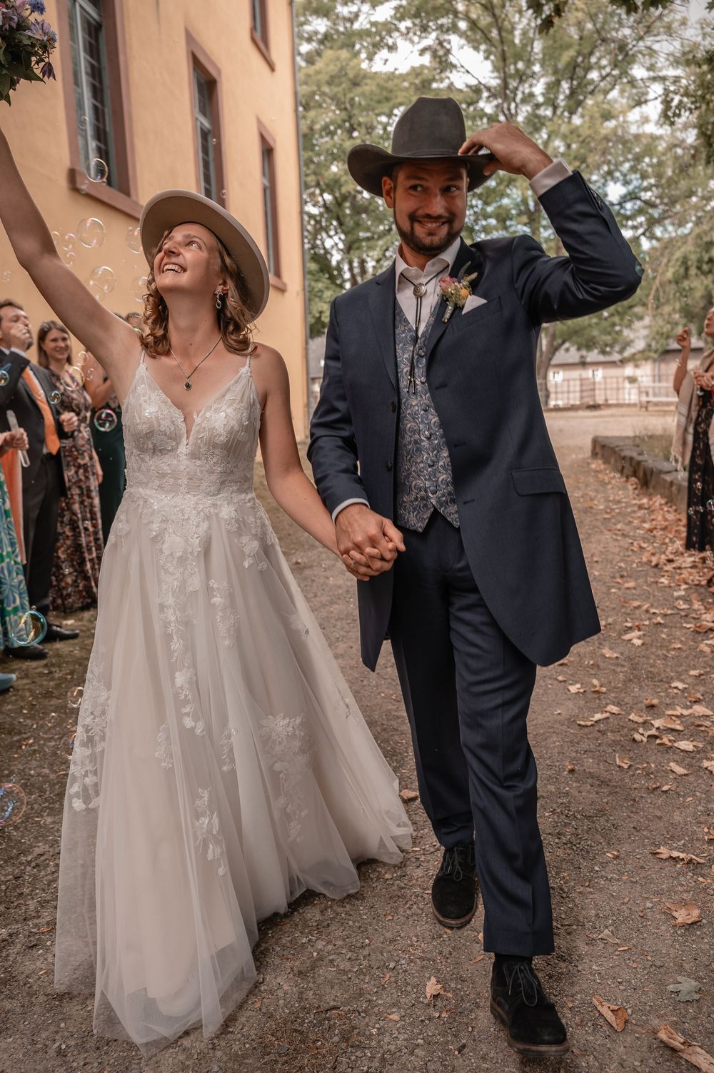 A newlywed couple walks together outside while guests throw confetti during their wedding celebration.