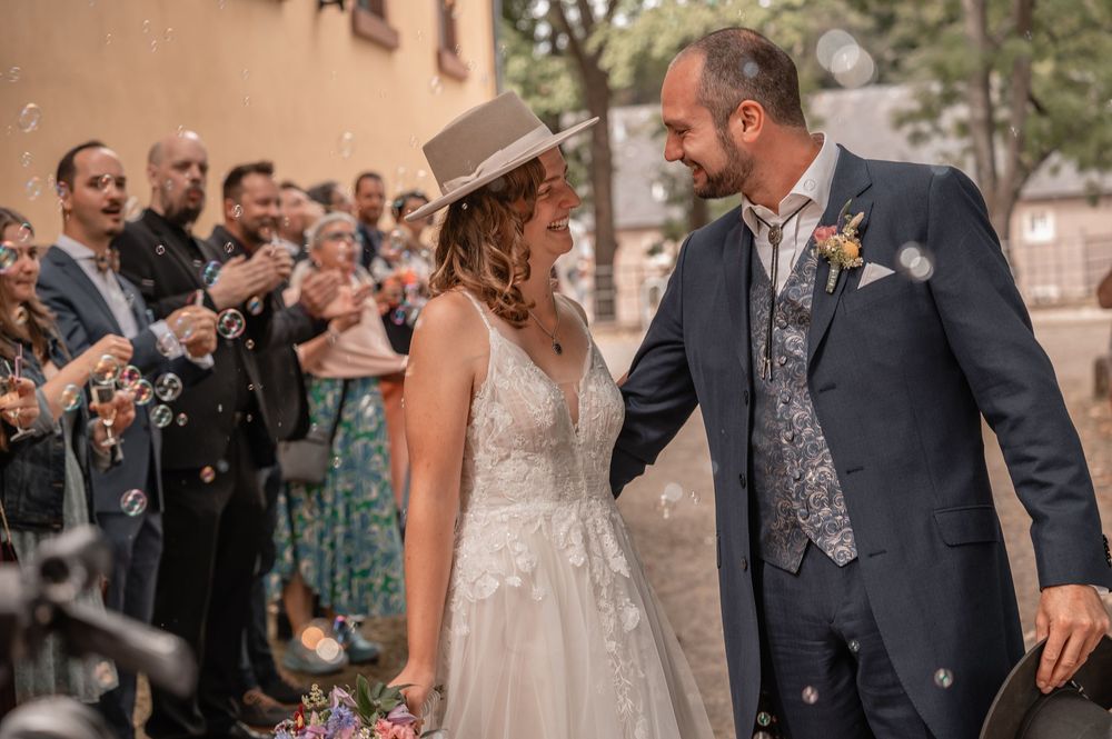 Newlyweds celebrate with guests as bubbles float through the air at an outdoor wedding ceremony.