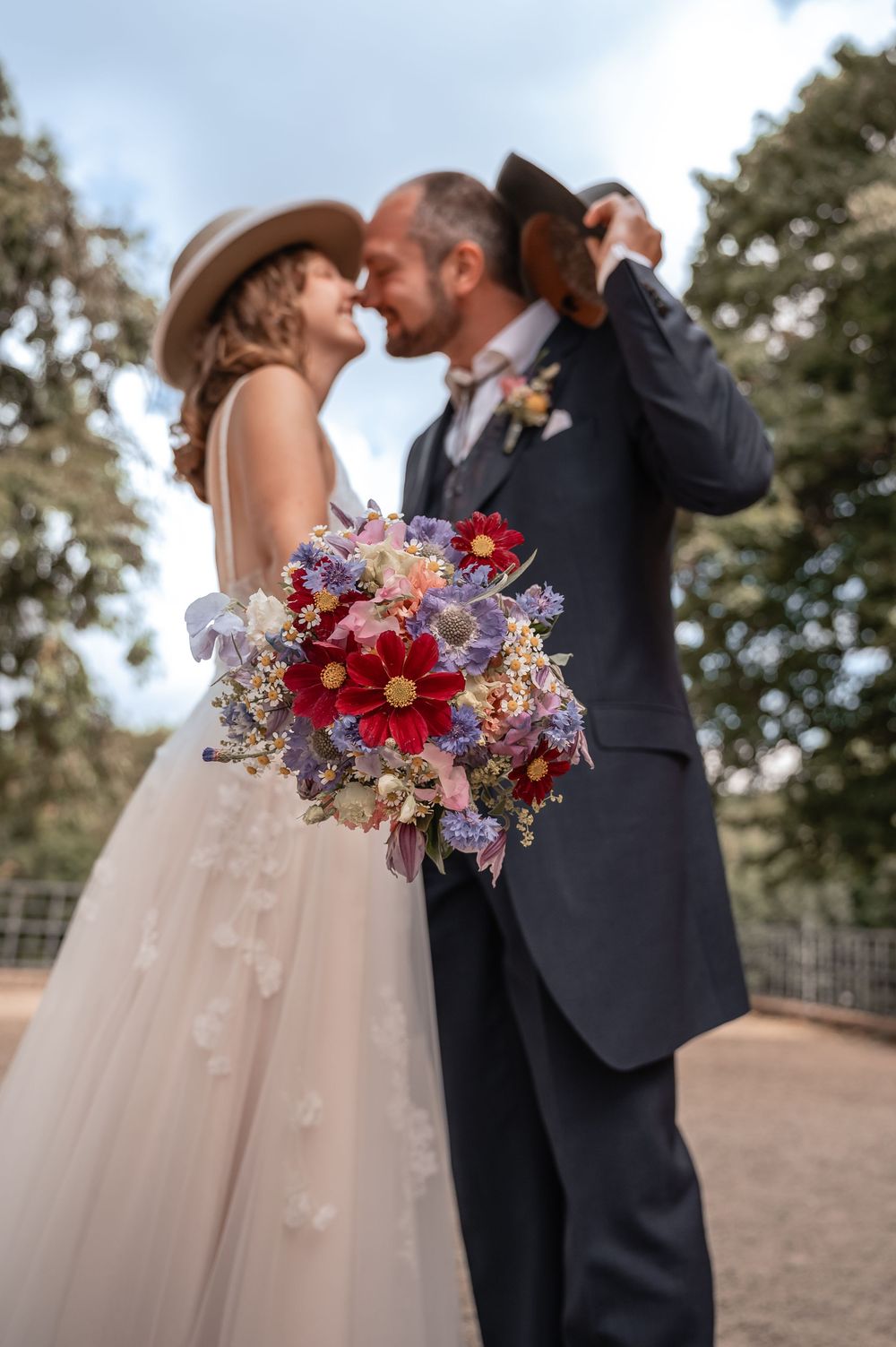 A romantic wedding moment captured with a stunning bouquet of red and purple flowers in the foreground.