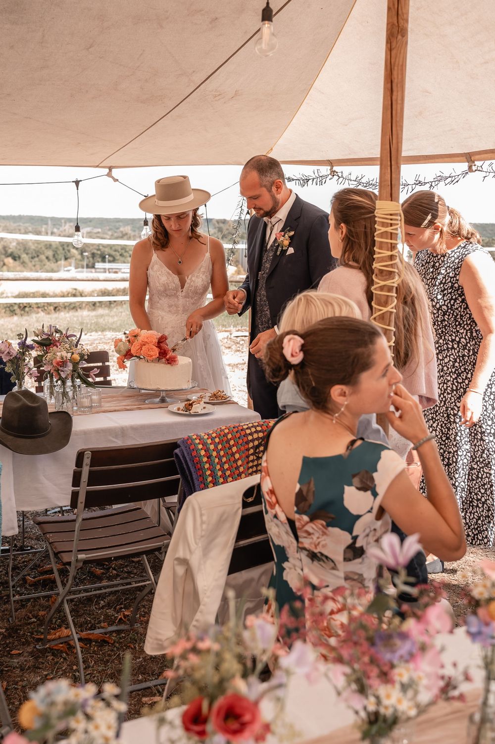 Wedding guests dance and celebrate under an elegant tent with pink floral arrangements decorating the tables.