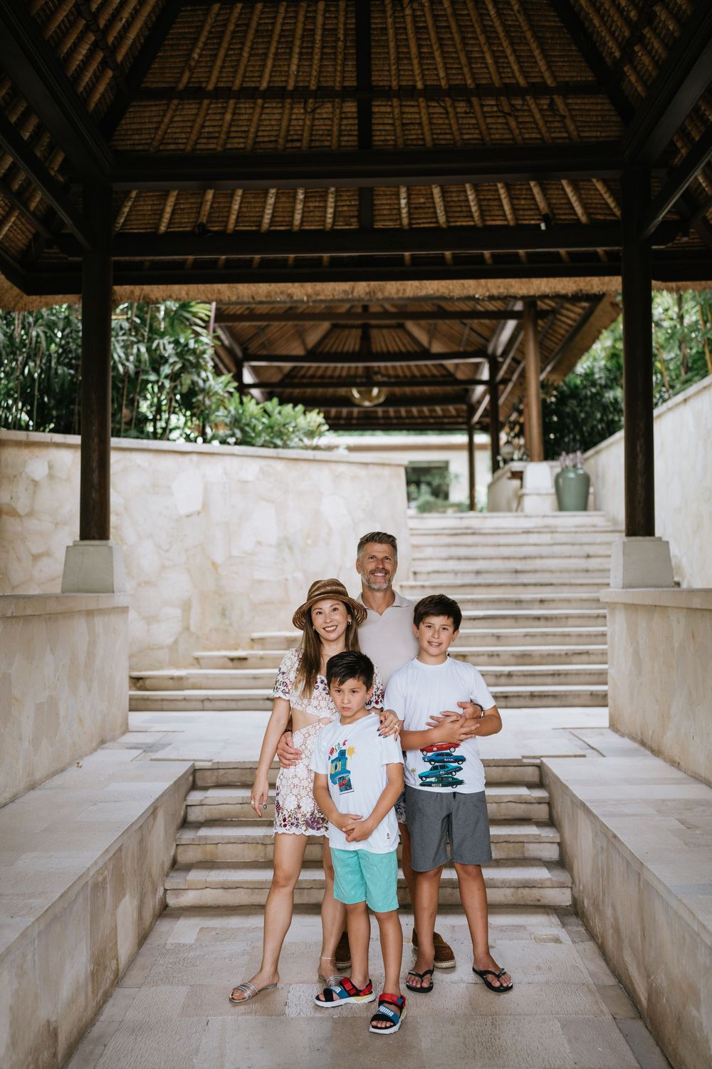A family poses together on stone steps under a traditional Balinese pavilion.