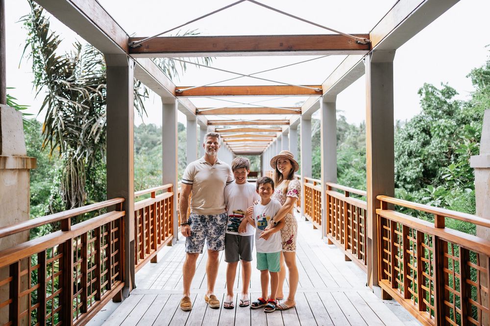 A family stands together on a wooden bridge walkway surrounded by tropical greenery.