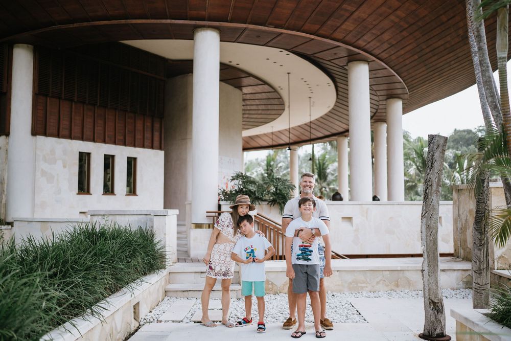 Family standing together under curved architectural columns surrounded by tropical landscaping.