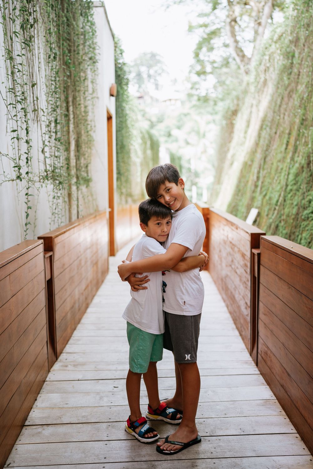 Two people sharing an embrace on a wooden walkway with hanging vines and greenery.