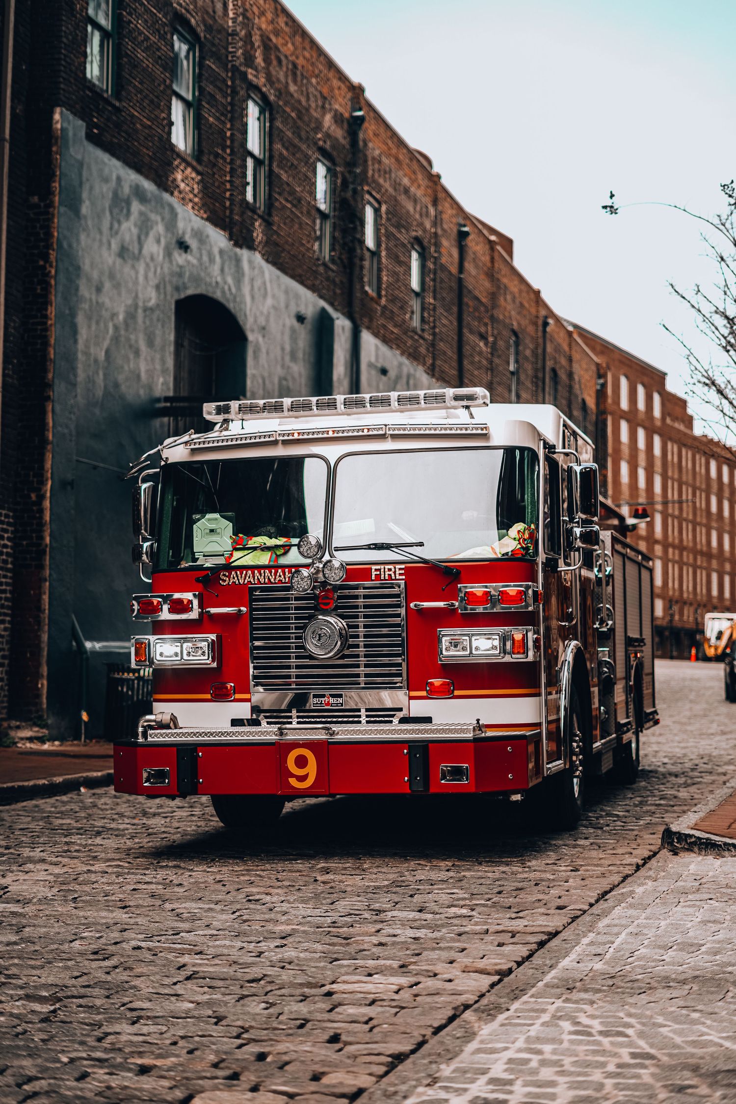 Red fire truck number 9 parked on cobblestone street beside brick buildings.