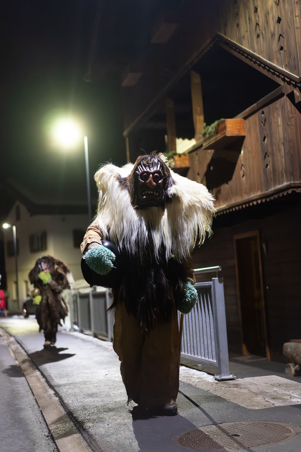 Traditional Krampus performers in dark costumes and masks run through snowy streets during a nighttime parade event.