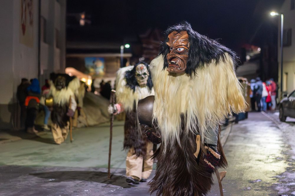 Traditional Kukeri performers wearing furry costumes and masks dance at a Bulgarian folklore festival at night.