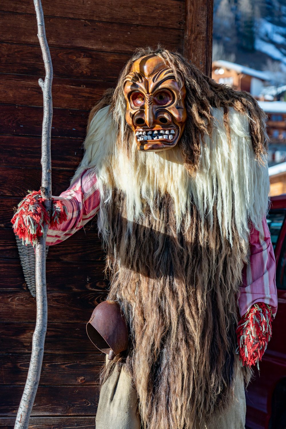 Traditional Alpine folklore masks with long white hair and grotesque features displayed on wooden wall at winter festival.