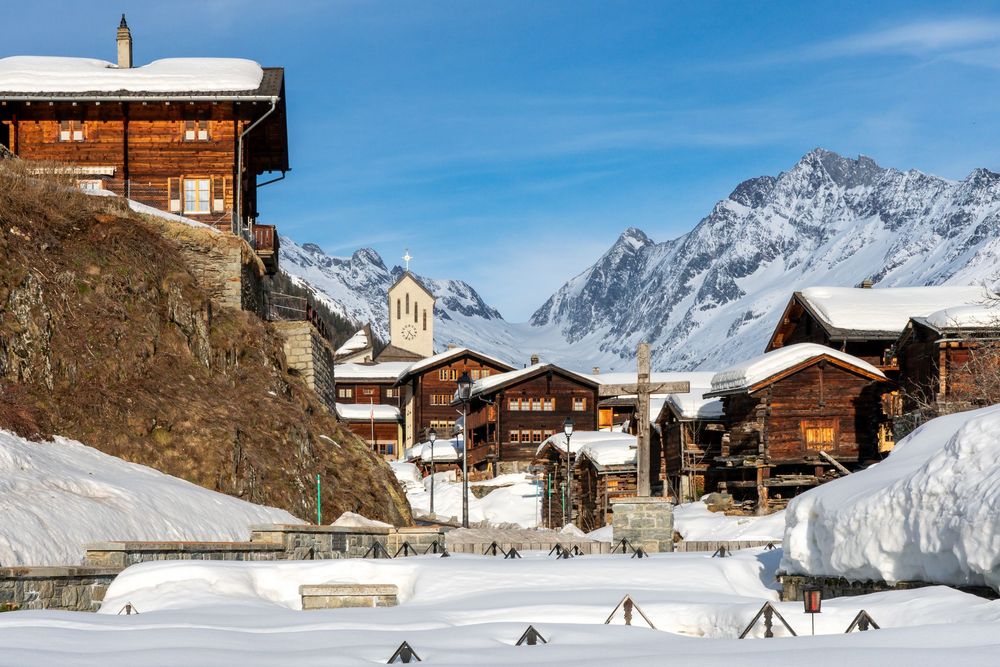 Snowy ski village in the Swiss Alps with traditional wooden chalets and mountain peaks in the background.