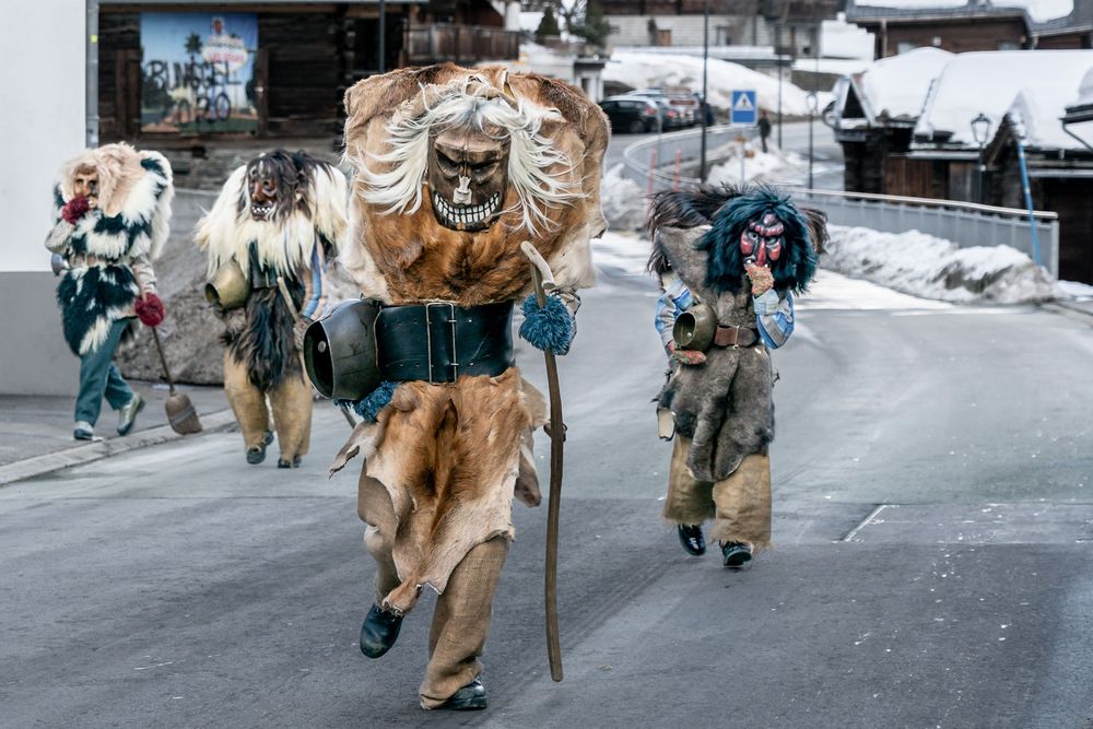 A happy golden retriever running and playing in the snow with people walking behind it.