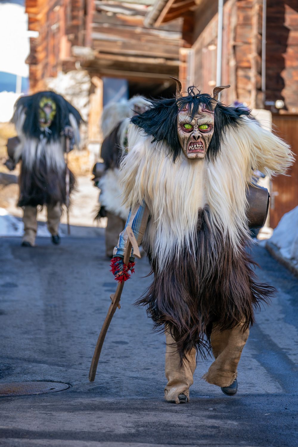 Traditional Krampus figure wearing fur costume performs in winter folklore festival on cobblestone street.