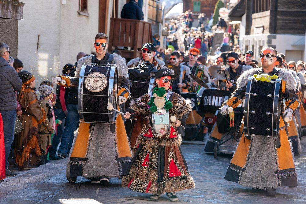 Festival participants in traditional medieval costumes parade through a crowded historic street during a cultural celebration.