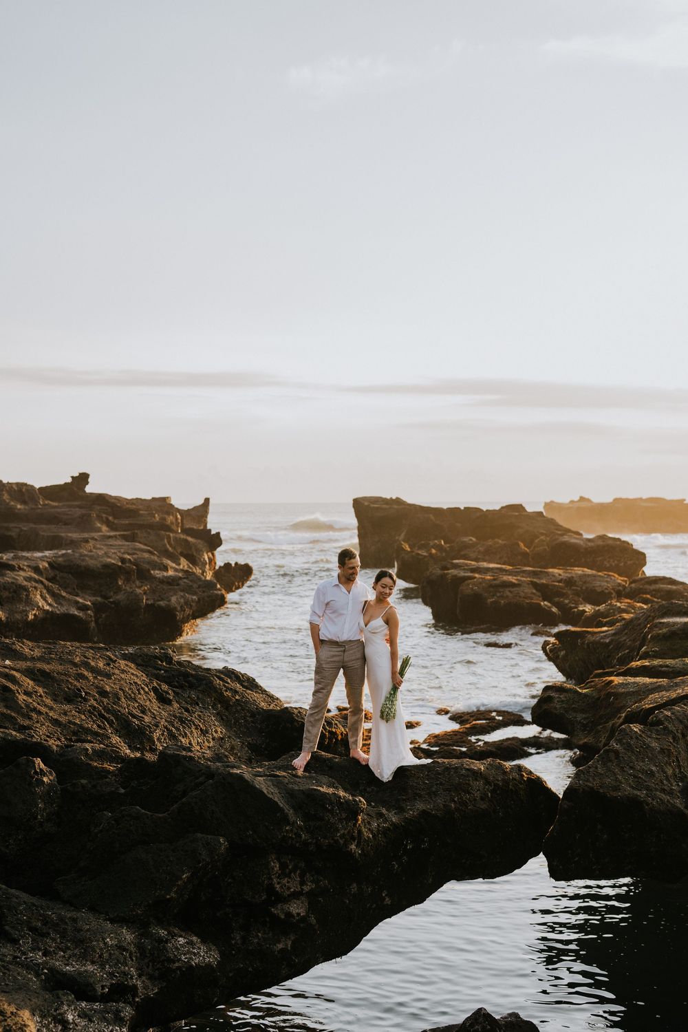 Romantic coastal photoshoot on dramatic rocky cliffs overlooking ocean at sunset.