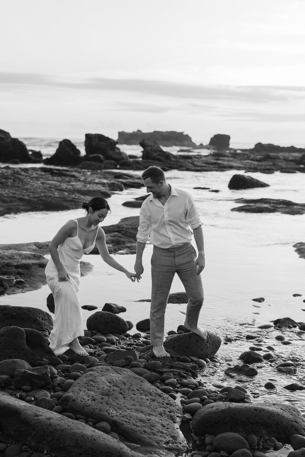 Black and white photo of couple carefully traversing rocky coastal terrain.