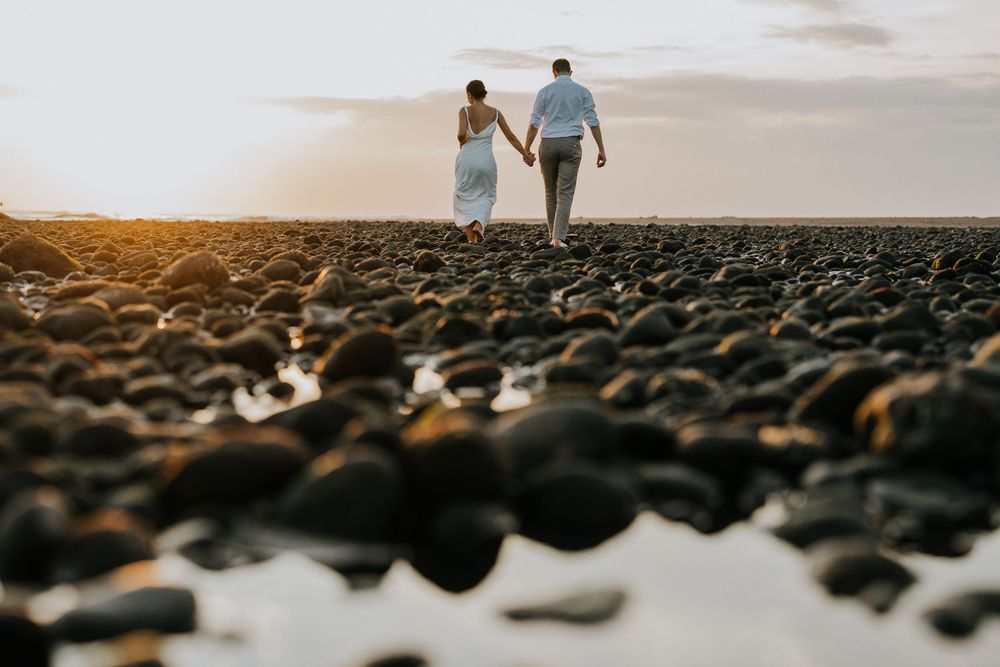 Silhouetted figures walking along rocky beach shoreline during golden hour.