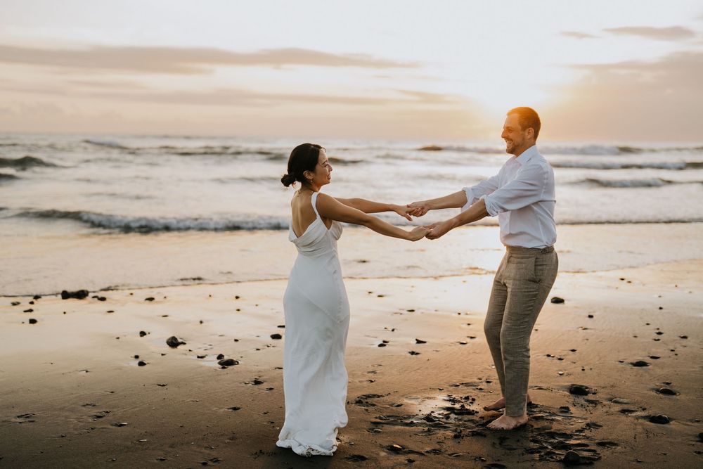 Couple dancing playfully on sandy beach during golden sunset hour.