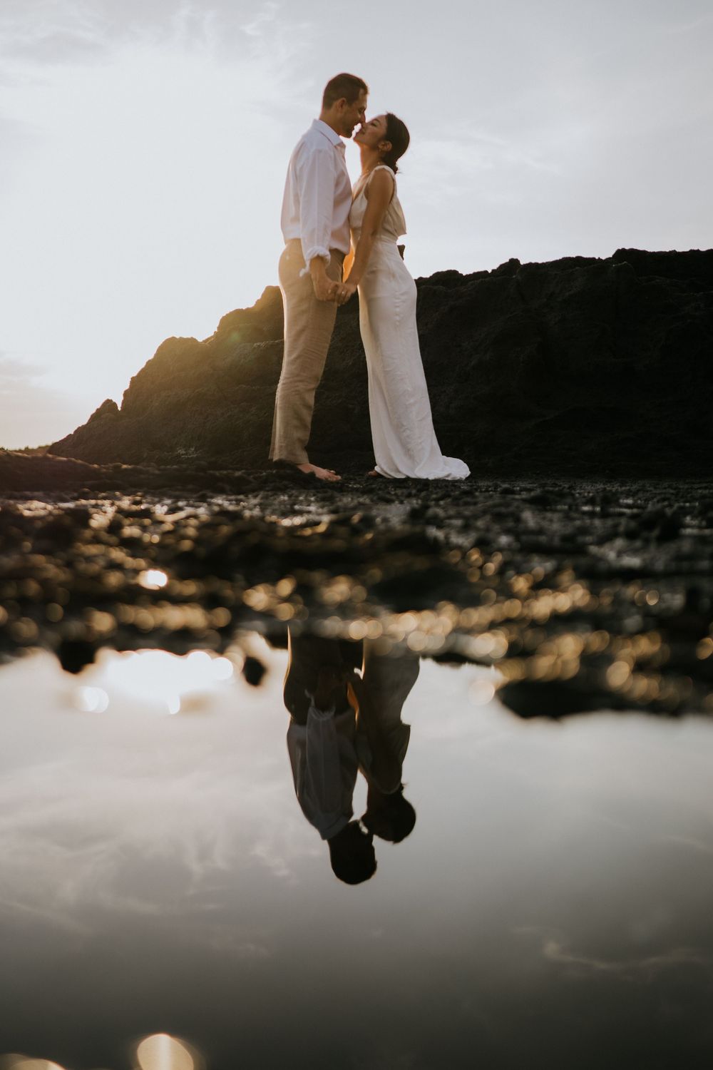 A couple's silhouette reflected in a tidal pool at sunset.