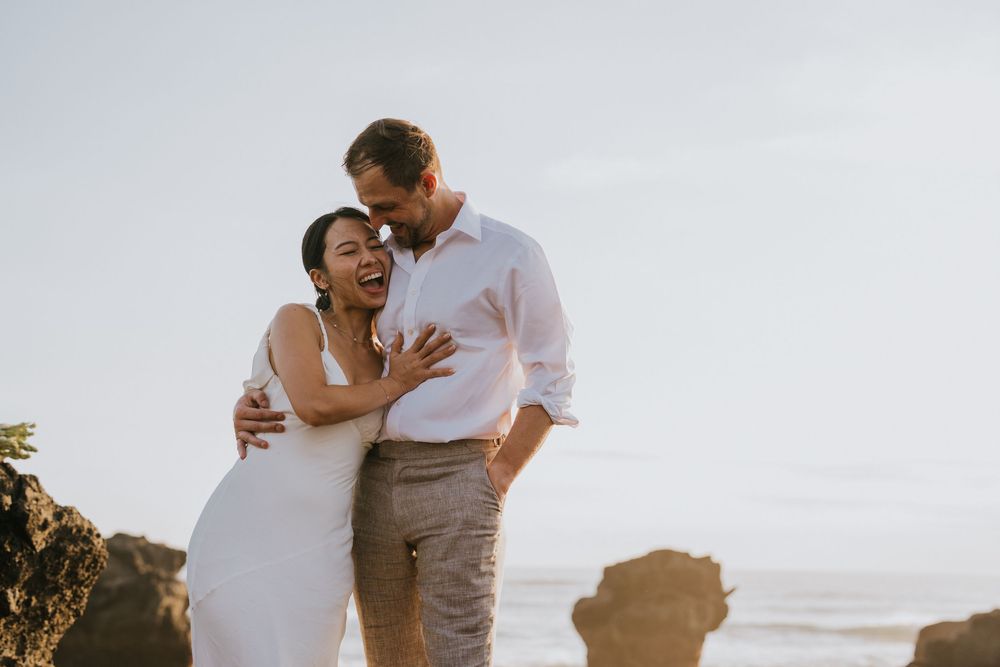 A couple embracing on a sunny beach in casual white attire.