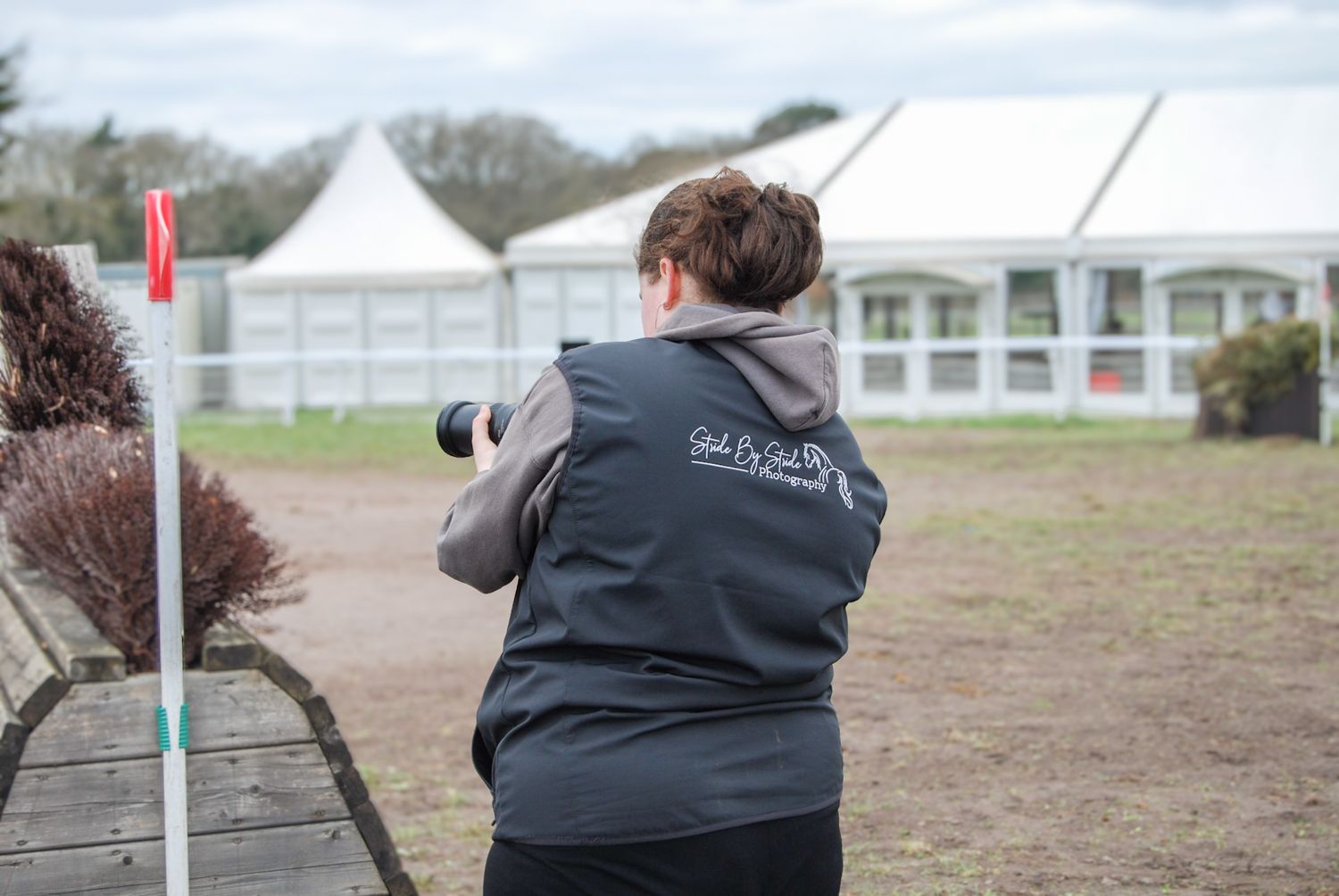 A photographer in a branded vest captures images at an outdoor equestrian event venue.