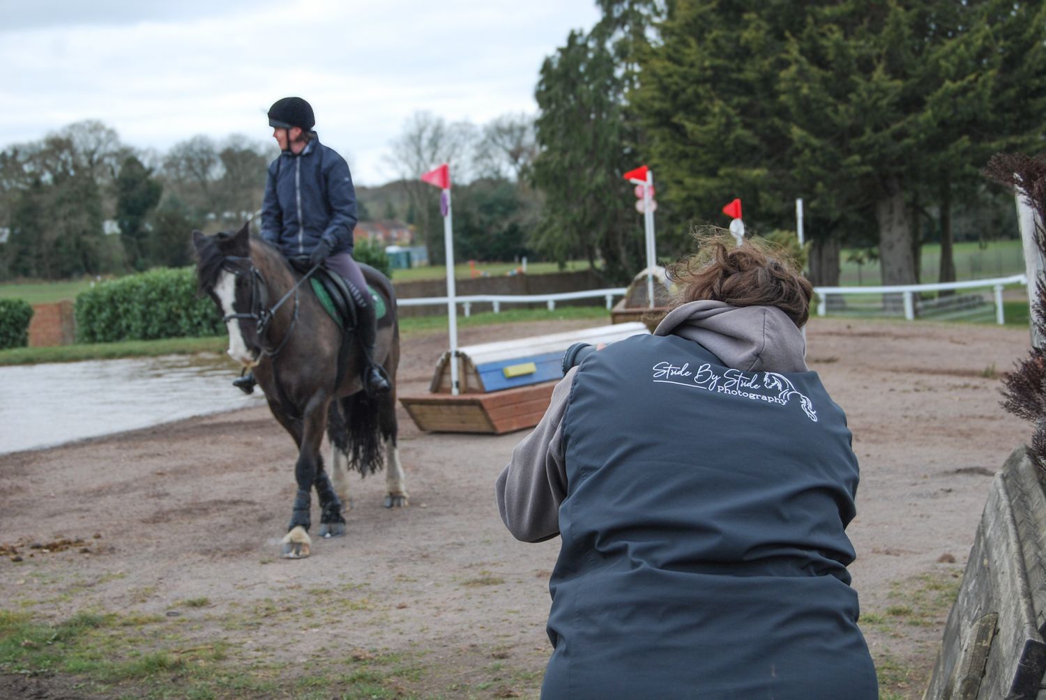 A photographer takes photos of a rider on horseback at an outdoor equestrian arena.