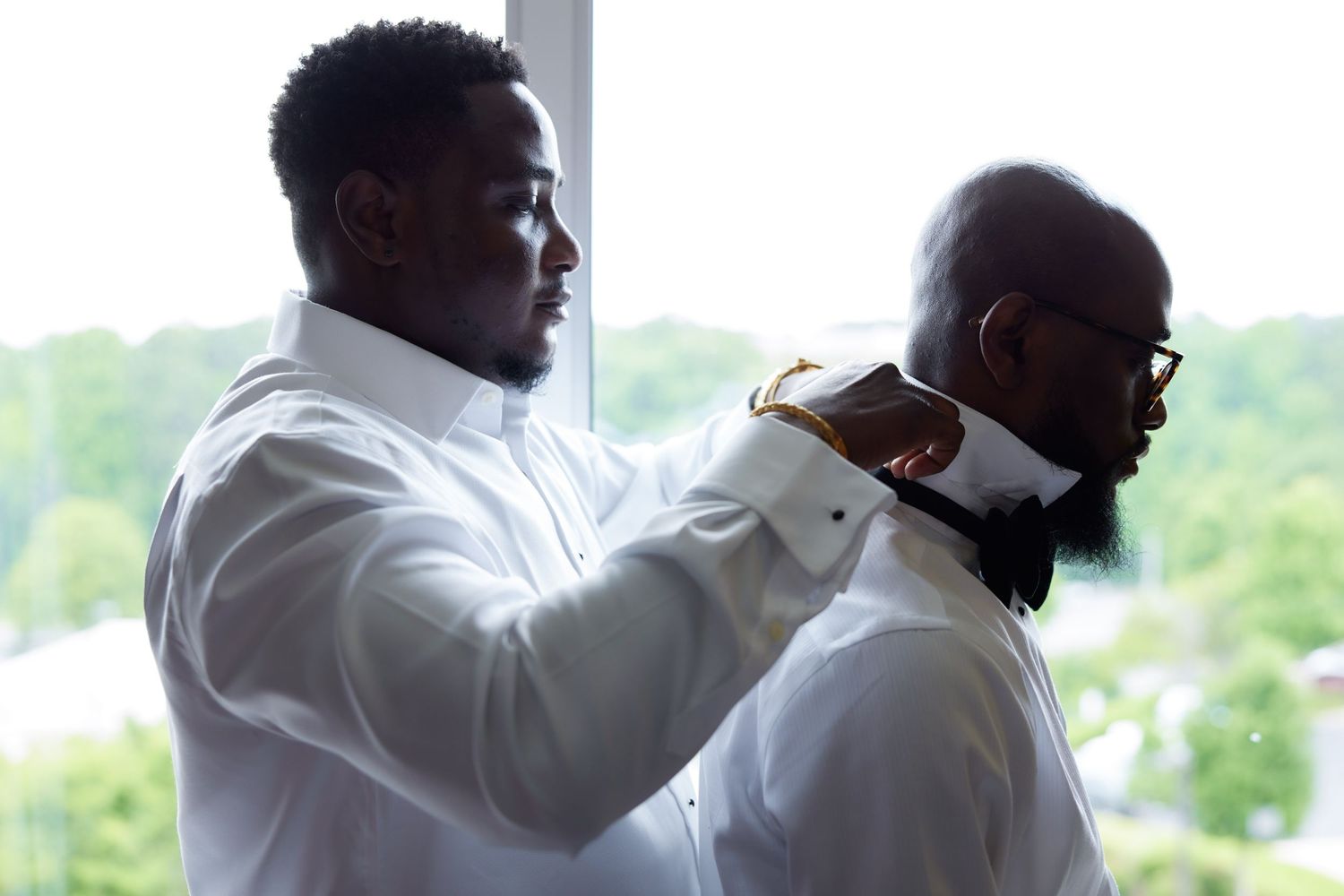 Four sequential photos showing a barber giving a bearded client a fresh haircut against a bright window background.