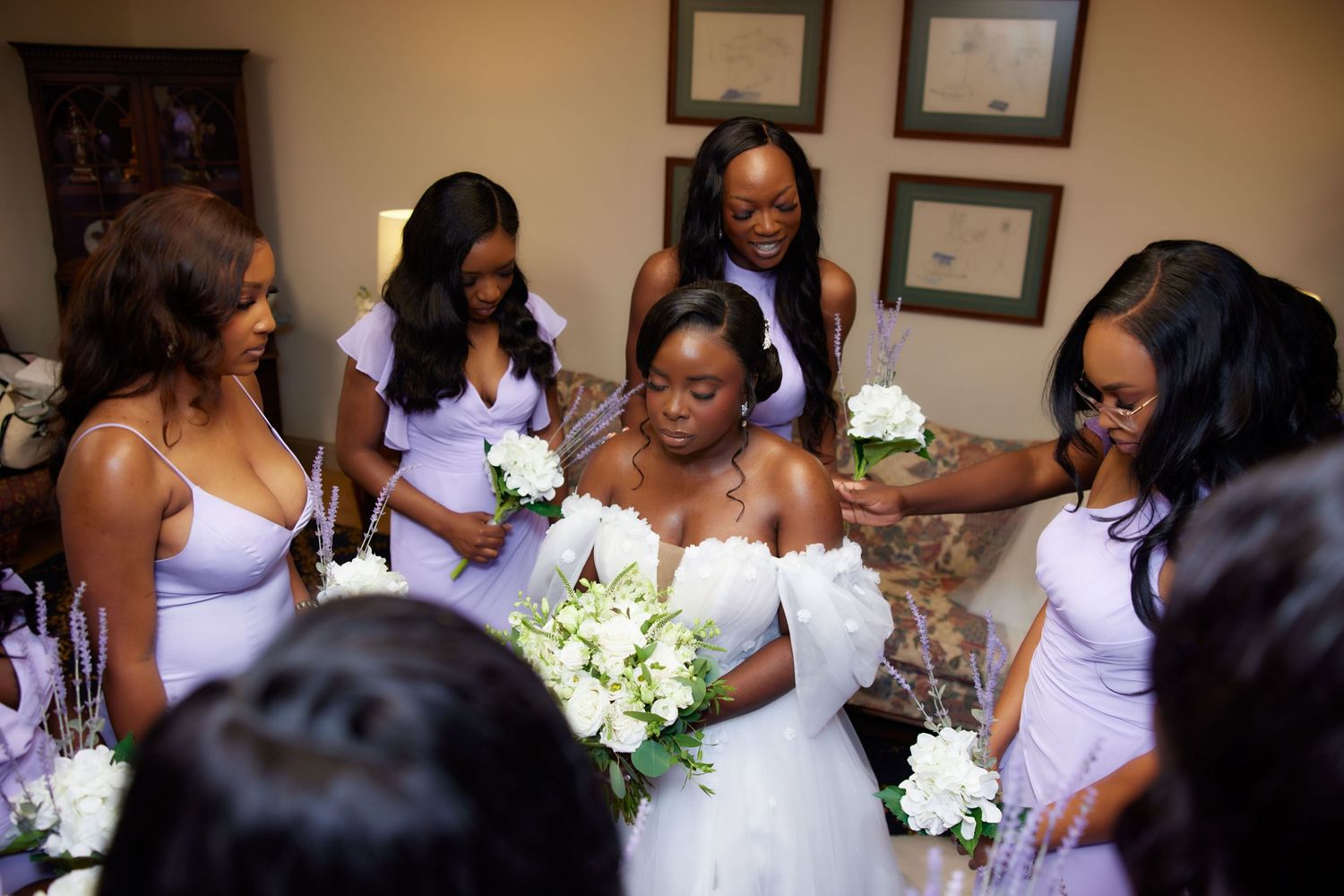 A joyful wedding party gathers in a dimly lit room with happy expressions and white floral bouquets.