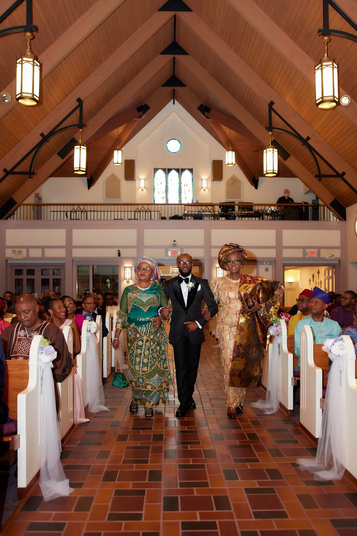 Panoramic view of a fashion show displaying elegant wedding dresses on mannequins inside a church hall with terracotta flooring.