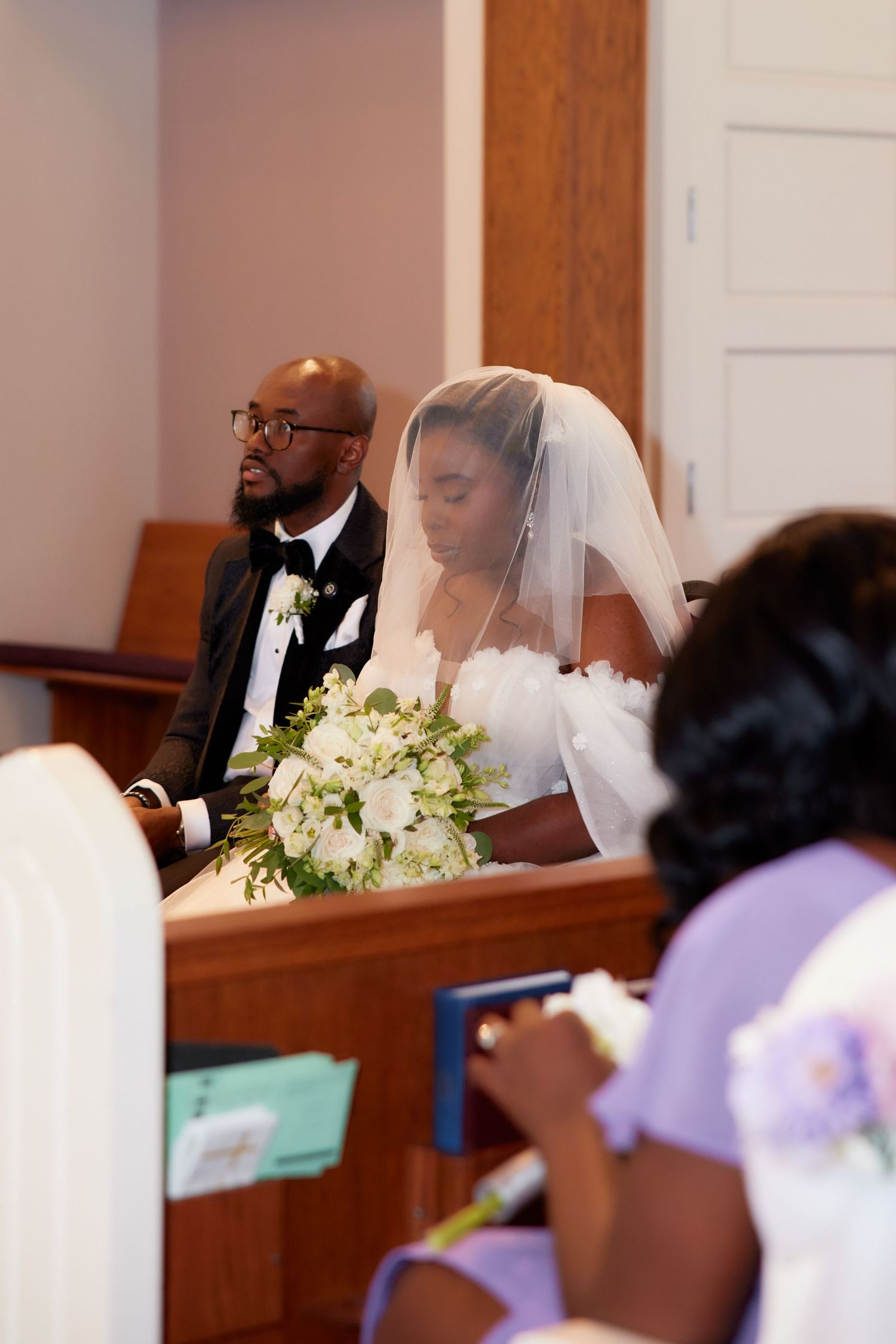 A wedding ceremony scene in a church with white floral bouquets and attendants in formal attire.