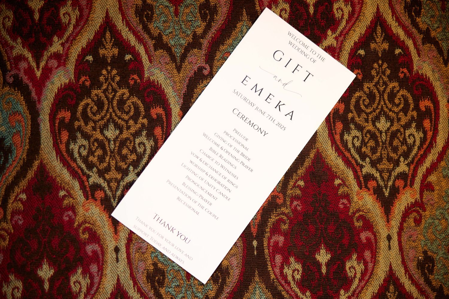 A white paper menu or card rests on top of an ornate burgundy and gold damask patterned fabric or wallpaper.