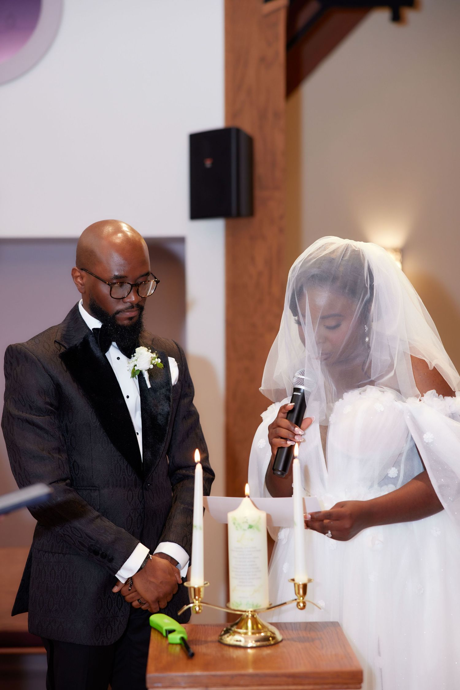 A couple in formal wedding attire lights a unity candle together during their marriage ceremony.