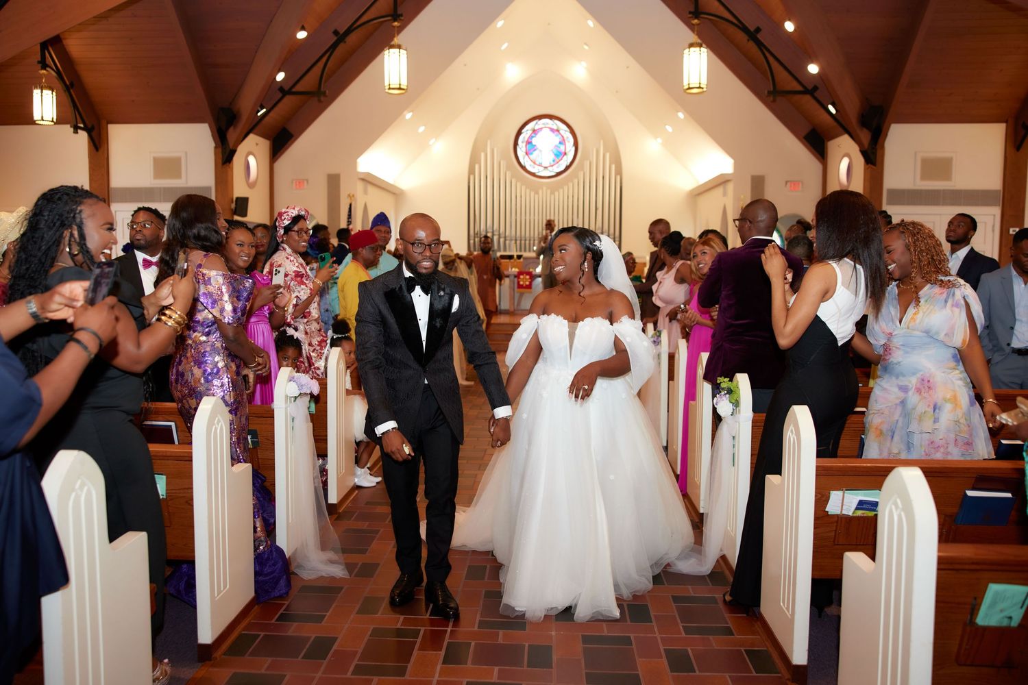 A wedding processional takes place in a traditional church with white pews and decorative lighting.