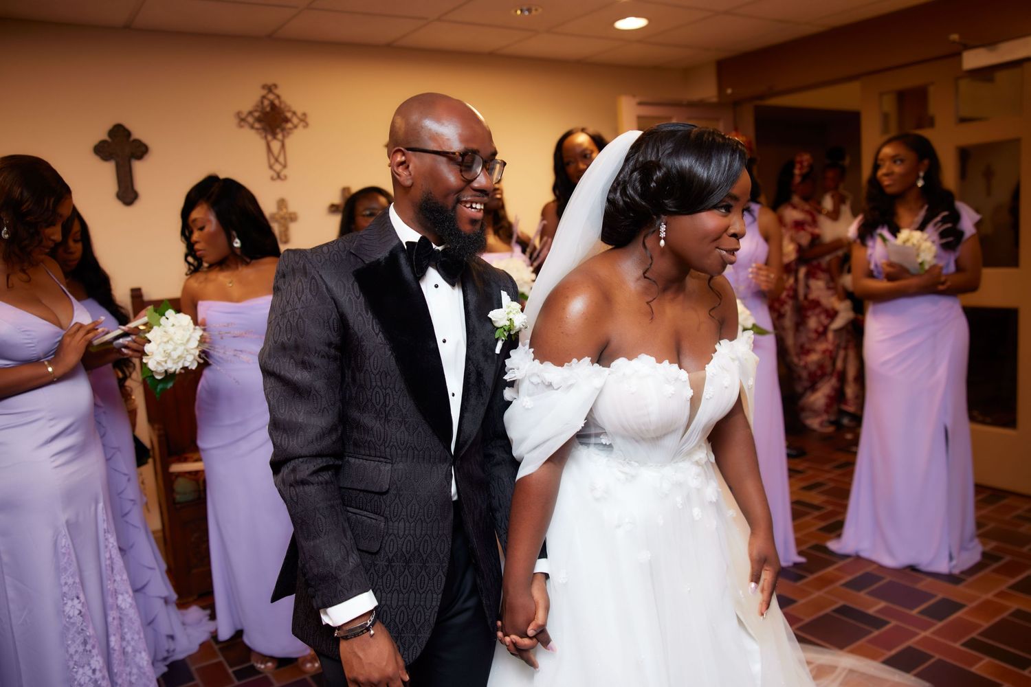 A large wedding party dances together at their reception in a hotel ballroom with pink uplighting around the room's perimeter.
