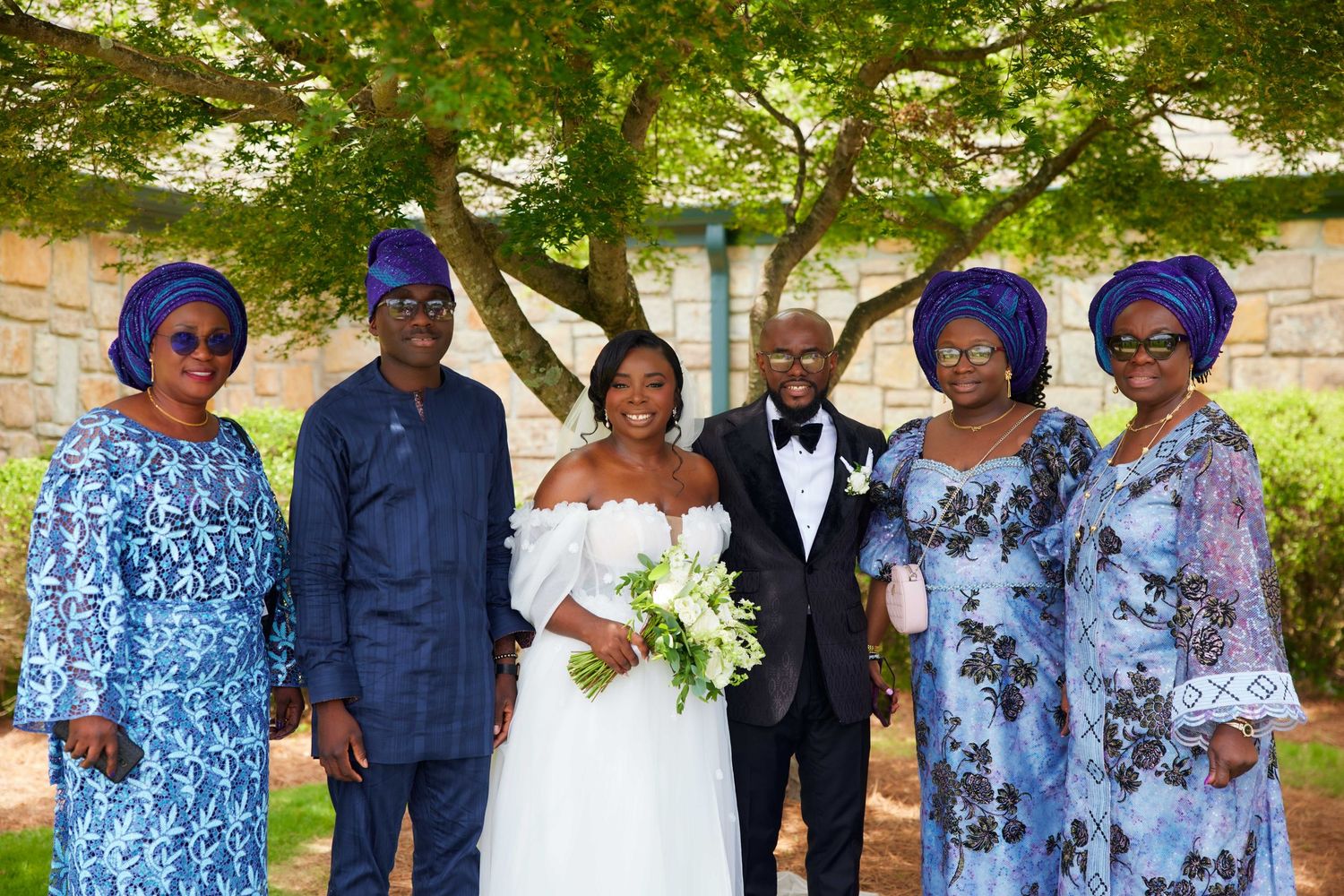 Wedding party in coordinated blue and white attire poses together for formal group photos in an outdoor garden setting.