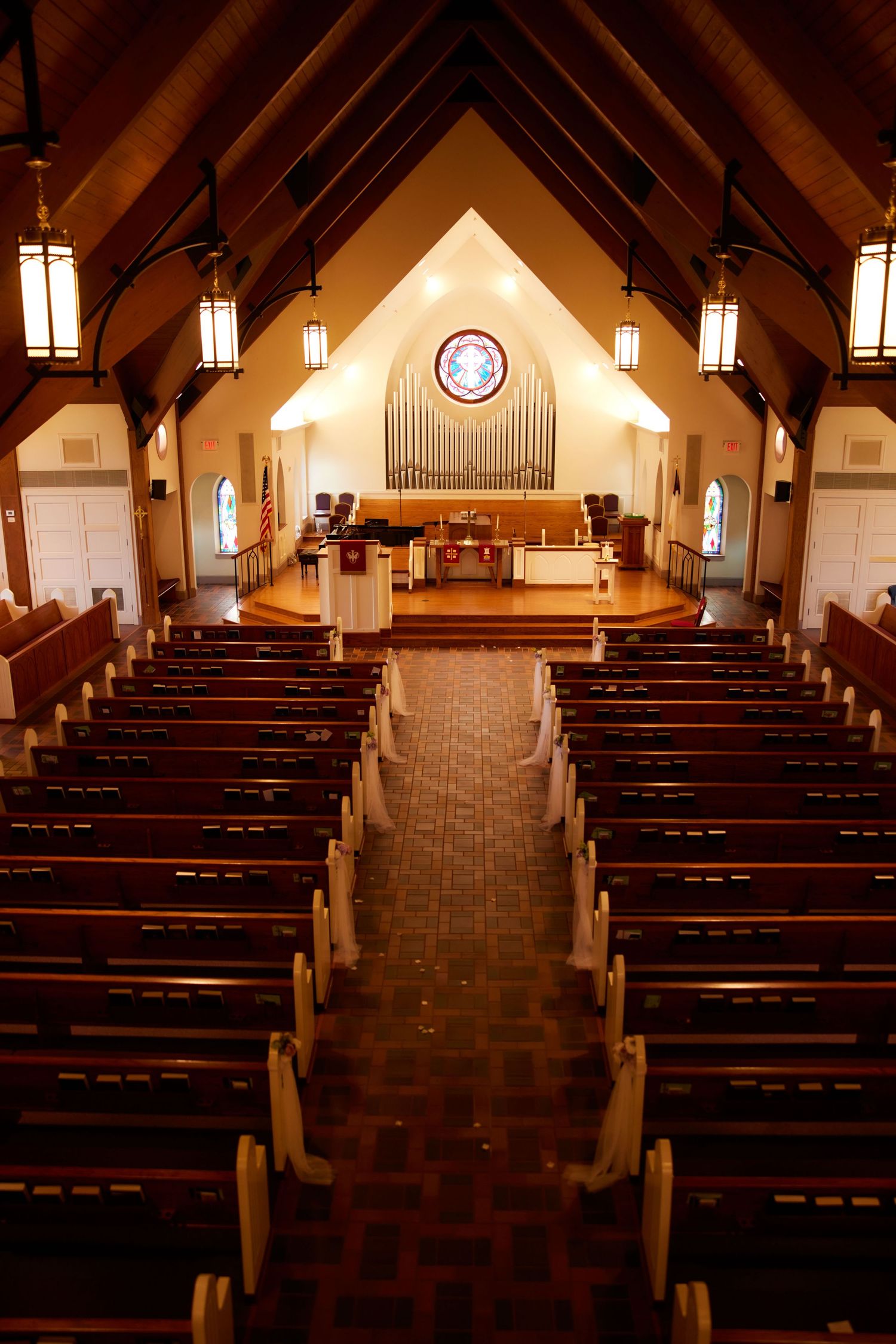 Interior panoramic view of a church sanctuary with wooden pews, vaulted ceiling, and hanging pendant lights.