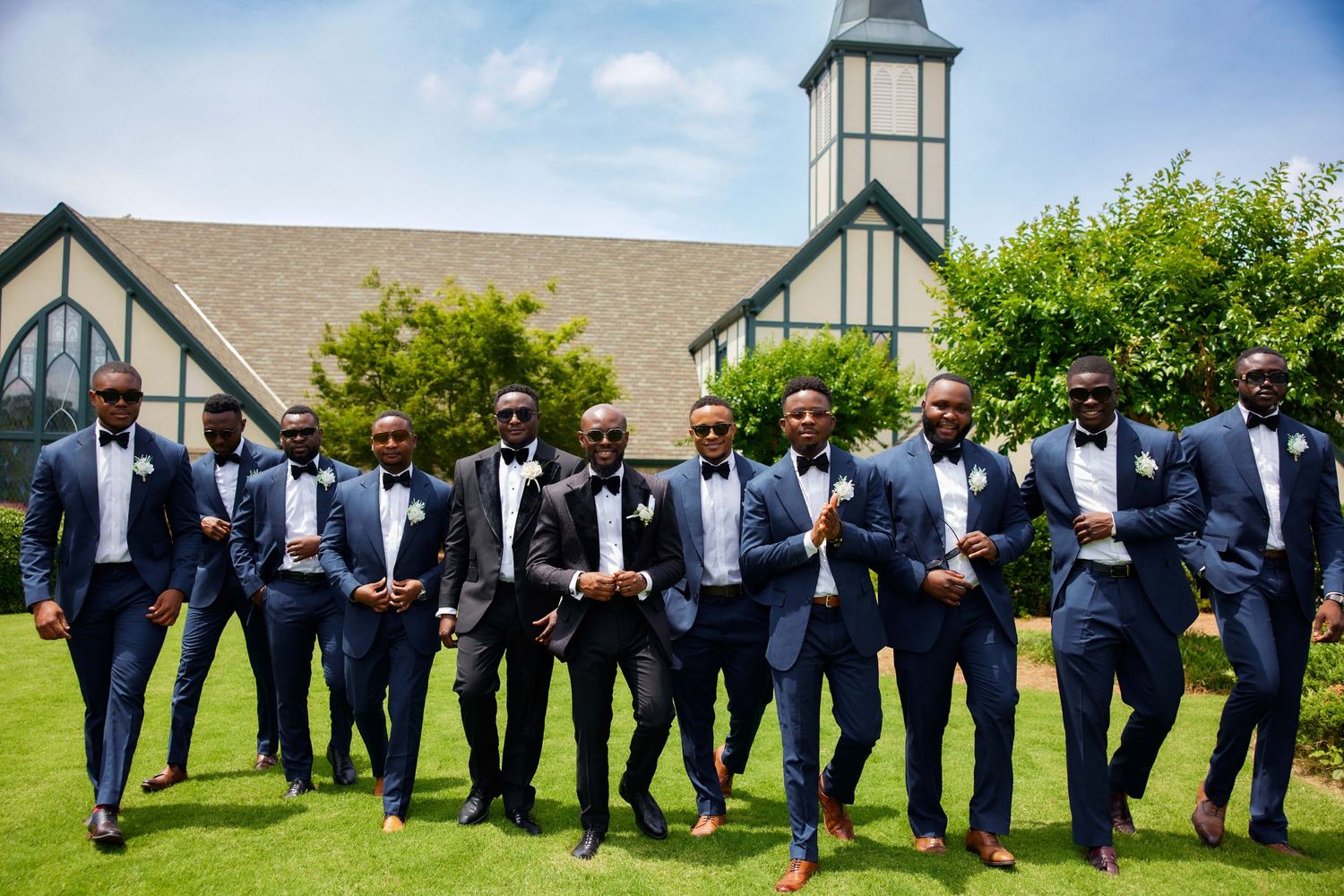 Wedding party members in formal navy suits form a line against a church building backdrop.