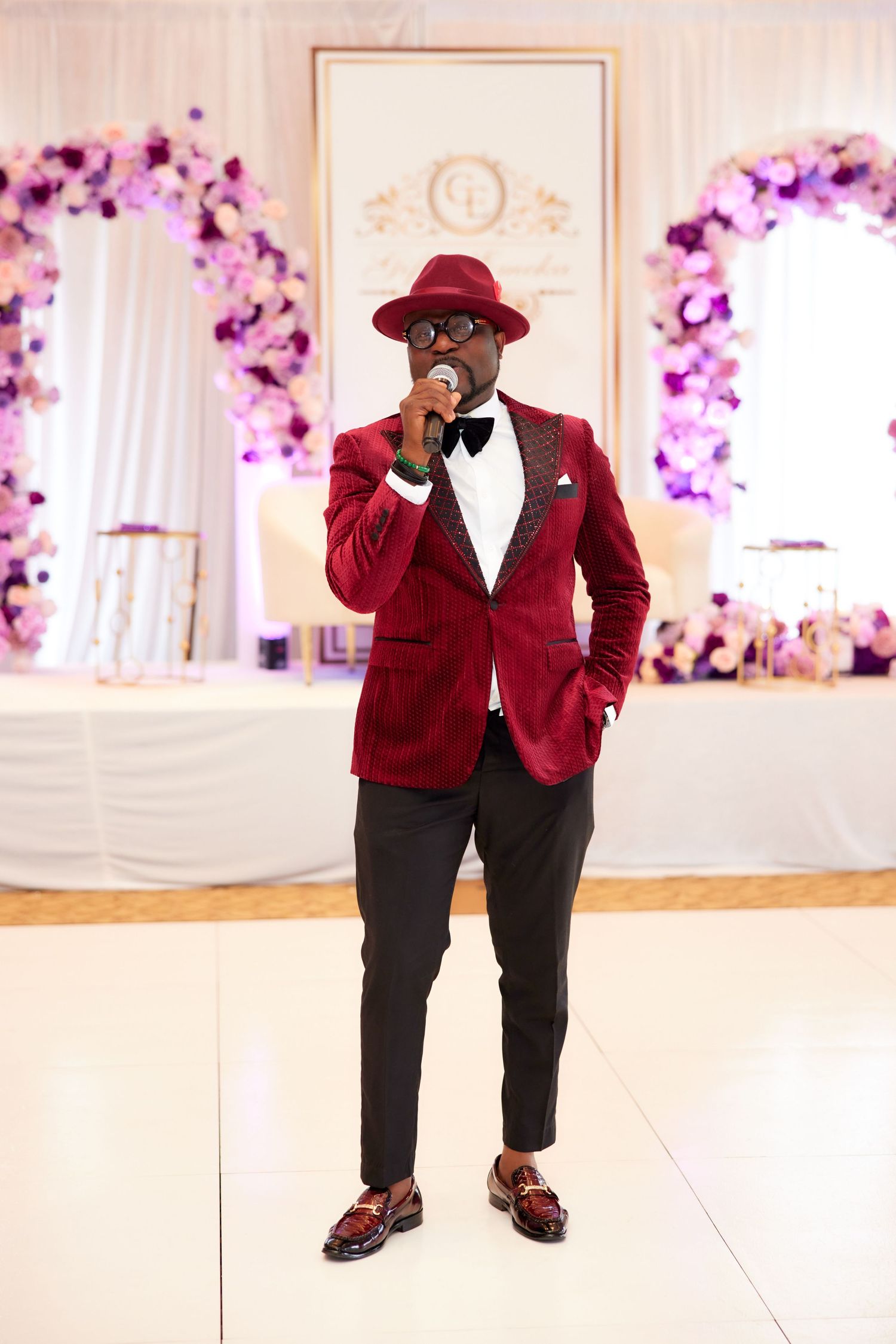 A person wearing a burgundy velvet blazer and black pants strikes multiple poses in an elegant wedding reception venue.