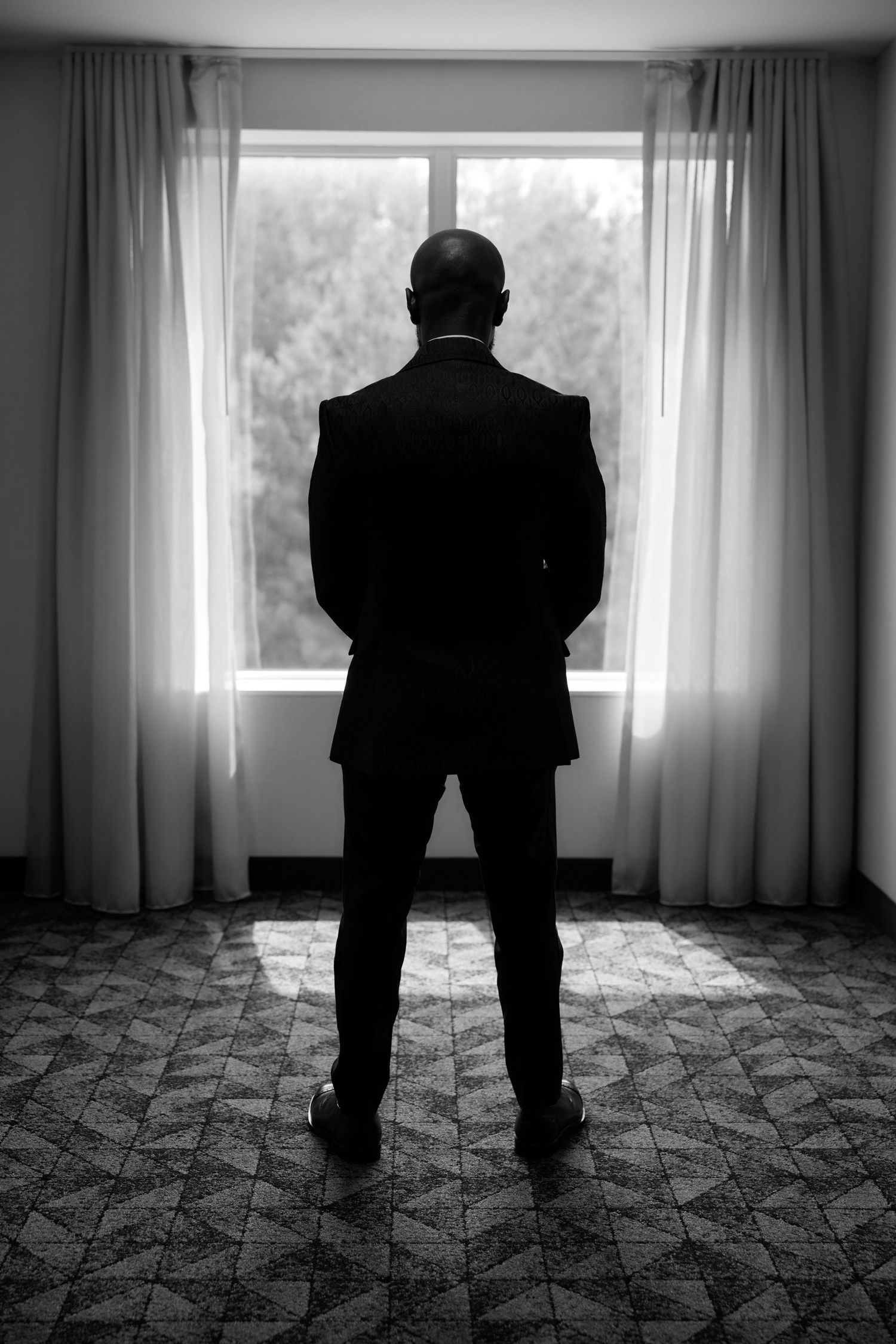 Black and white photo series showing a silhouetted figure standing against bright windows with curtains and patterned carpet.