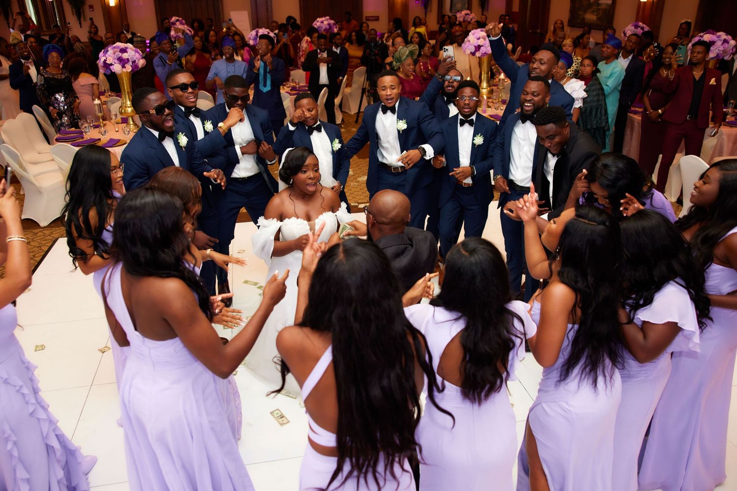 Large group of people celebrating at an indoor reception event with white and purple attire.