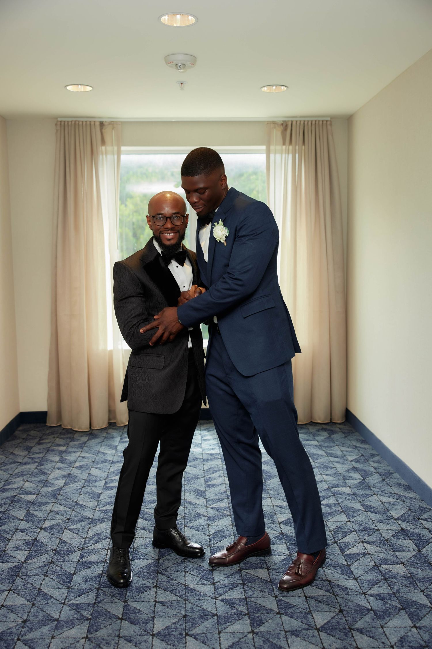 Two men in suits playfully interacting in a room with patterned carpet and light curtains in a sequence of photos.