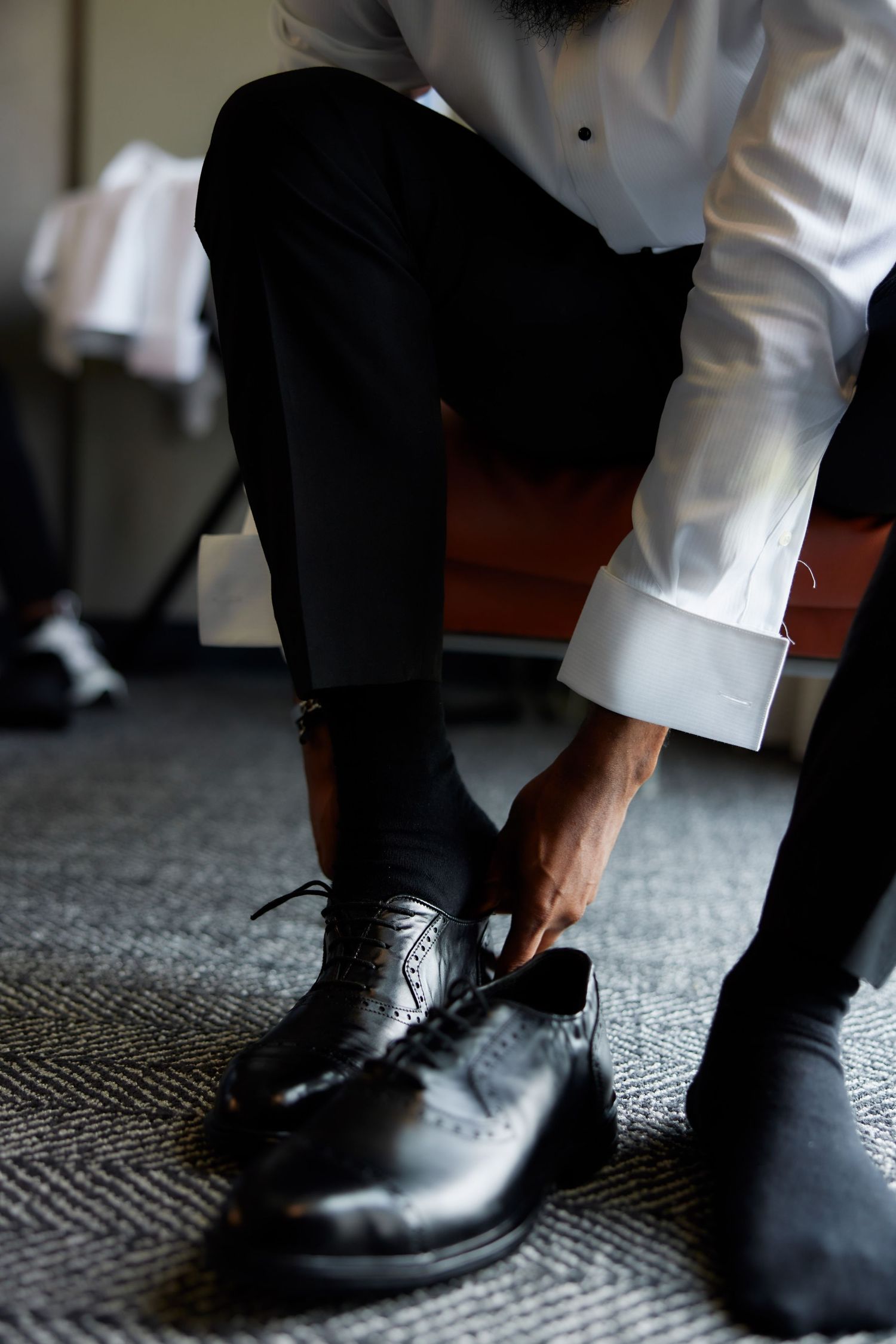 Someone in formal attire ties sleek black leather dress shoes while wearing dark trousers and white shirt.