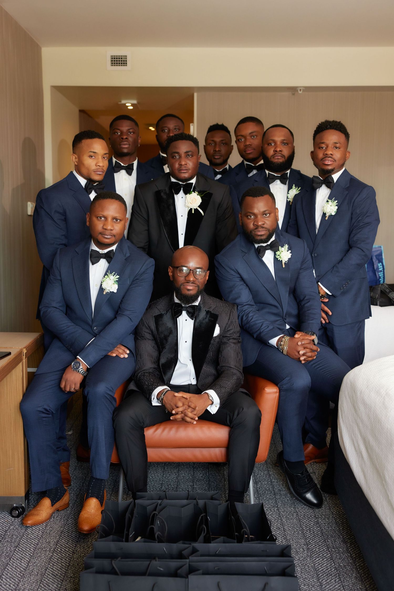 Groomsmen in matching navy suits and black bow ties posing together in a hotel room for a formal wedding photo.