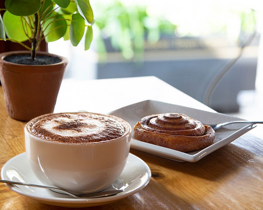 Coffee cups and potted plants on wooden table in cafe setting.