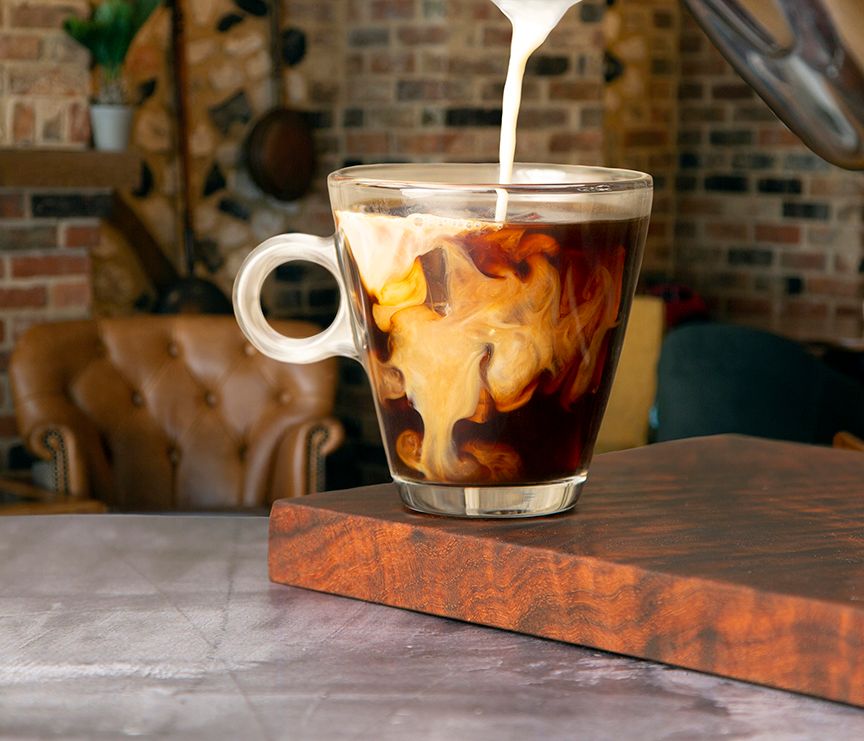 Overhead view of an iced coffee drink in a glass cup on a rustic wooden table.